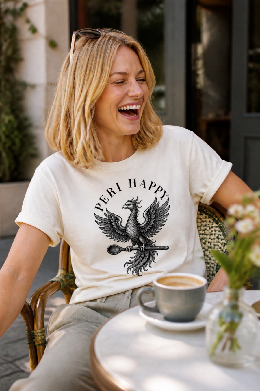 Woman laughing at a cafe table in the Phoenix Tee with sleeves rolled, showing the relaxed drape